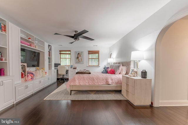 bedroom featuring an office area, dark wood-type flooring, arched walkways, and a ceiling fan