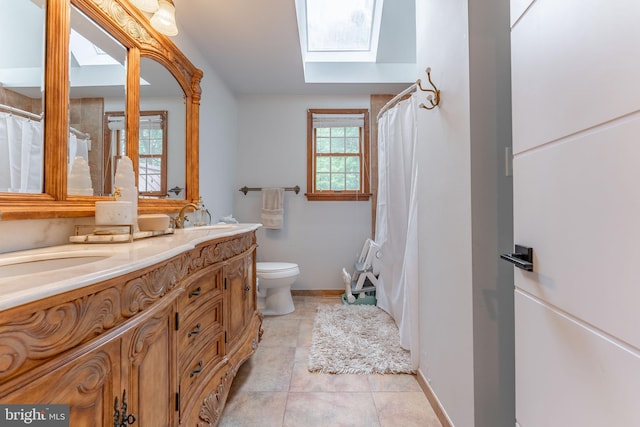 bathroom with a skylight, toilet, double vanity, baseboards, and tile patterned floors