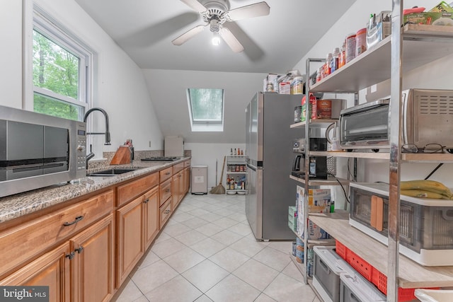 kitchen featuring a sink, stainless steel appliances, a skylight, light stone counters, and light tile patterned flooring