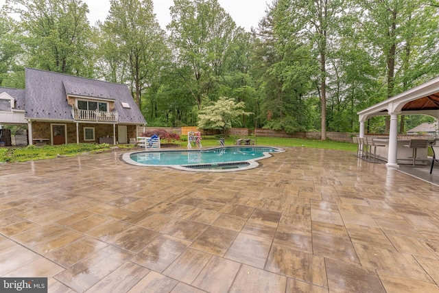 view of pool with a patio area, a fenced backyard, view of scattered trees, and a gazebo