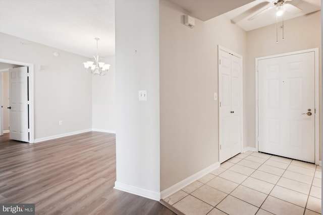 foyer entrance featuring baseboards, light wood finished floors, and ceiling fan with notable chandelier