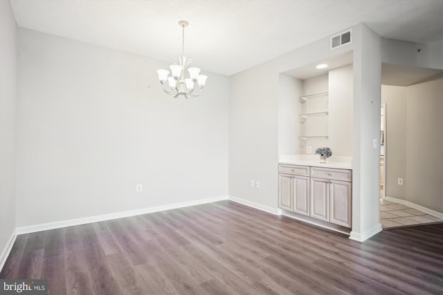 unfurnished dining area with baseboards, a notable chandelier, wood finished floors, and visible vents