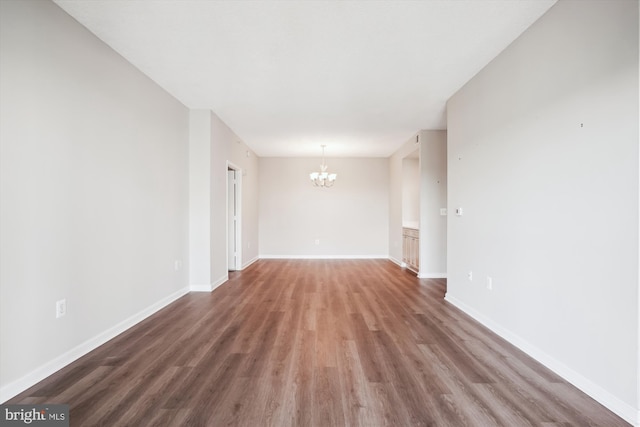 unfurnished room featuring baseboards, wood finished floors, and a chandelier