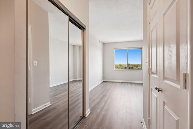 unfurnished bedroom featuring baseboards, wood finished floors, visible vents, and a closet