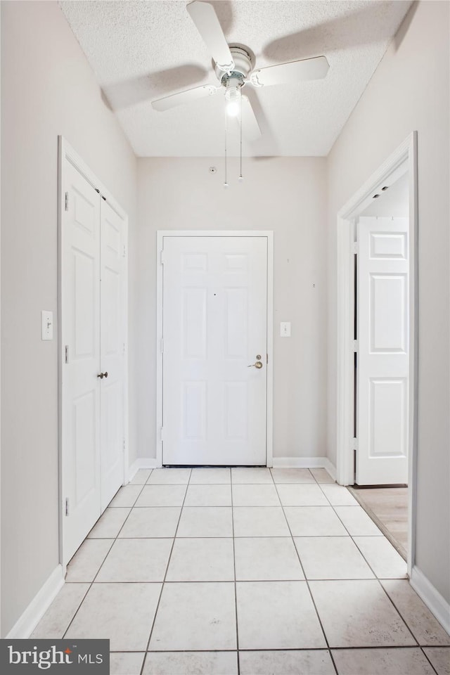 interior space featuring a ceiling fan, baseboards, a textured ceiling, and light tile patterned floors