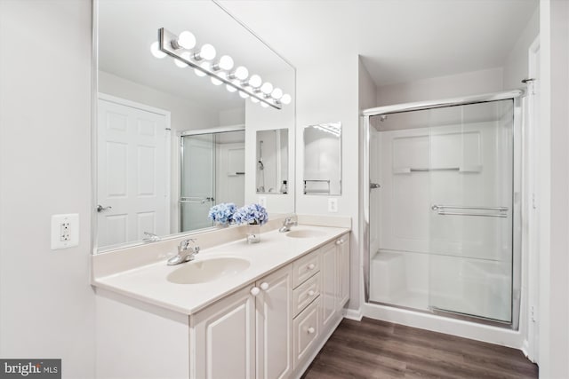 bathroom featuring double vanity, a shower stall, wood finished floors, and a sink