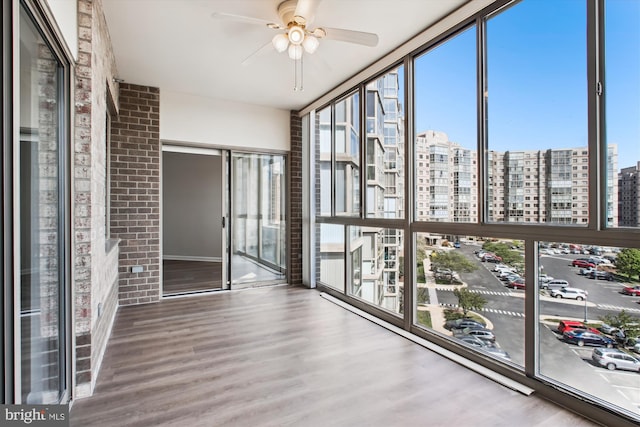 unfurnished sunroom with brick wall, wood finished floors, floor to ceiling windows, and a view of city