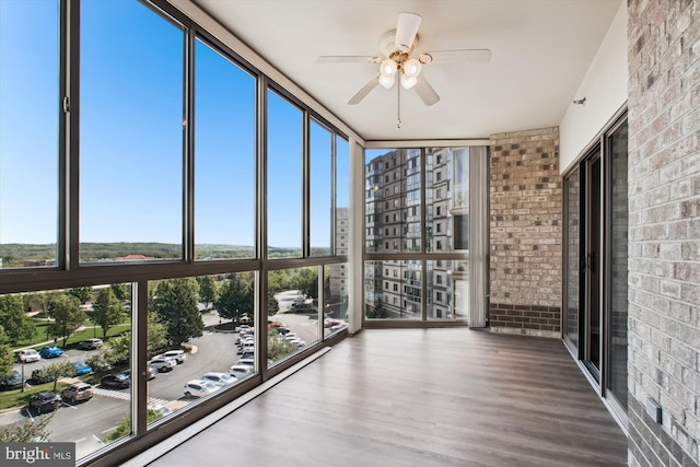 unfurnished sunroom with brick wall, a wealth of natural light, wood finished floors, and a wall of windows