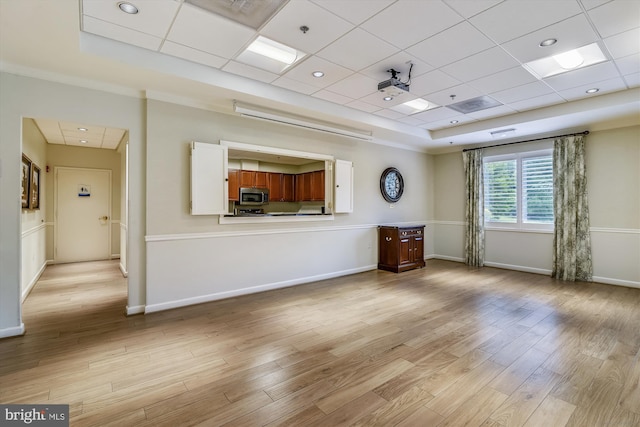 interior space with baseboards, light wood finished floors, and a raised ceiling