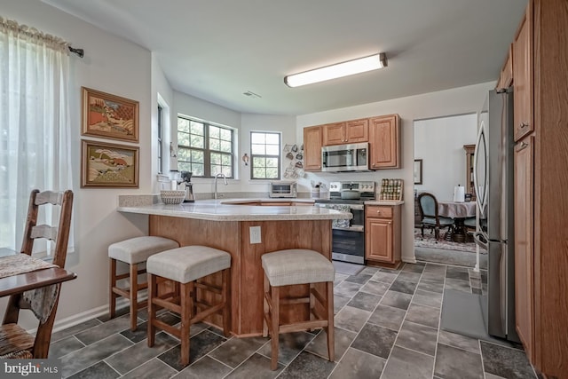 kitchen with a kitchen bar, stainless steel appliances, light countertops, and a peninsula