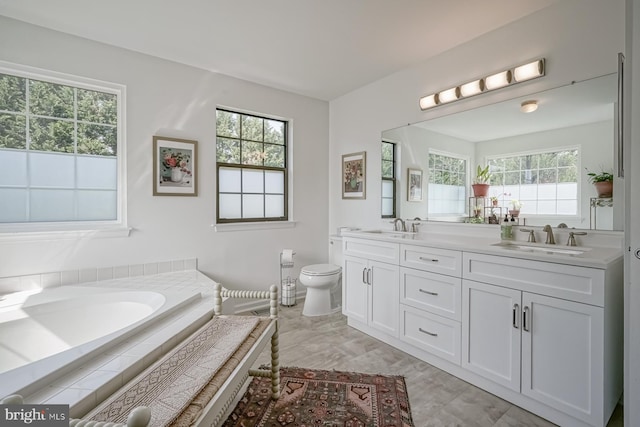bathroom featuring toilet, a bath, double vanity, and a sink