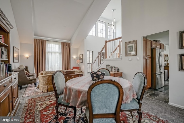 dining area featuring a high ceiling, stairs, and dark colored carpet