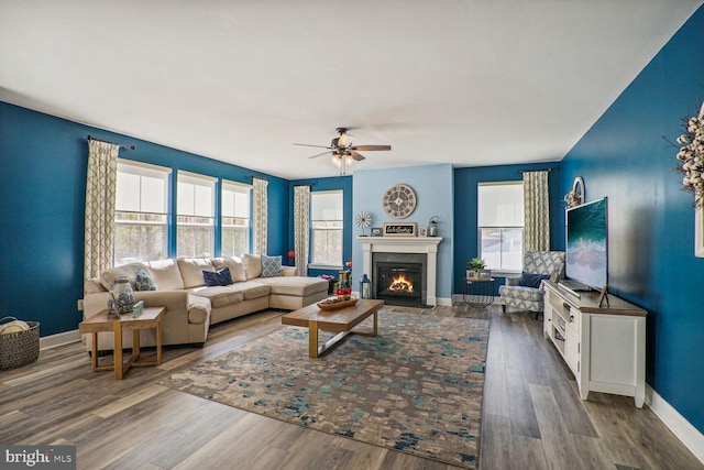 living room featuring baseboards, ceiling fan, a glass covered fireplace, and wood finished floors