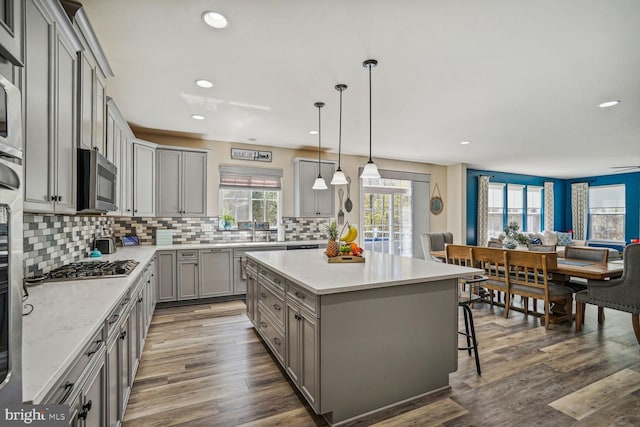 kitchen with a breakfast bar area, gray cabinets, a center island, stainless steel appliances, and backsplash