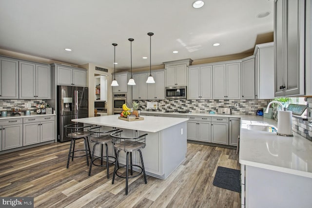 kitchen with appliances with stainless steel finishes, a sink, gray cabinets, tasteful backsplash, and a kitchen island