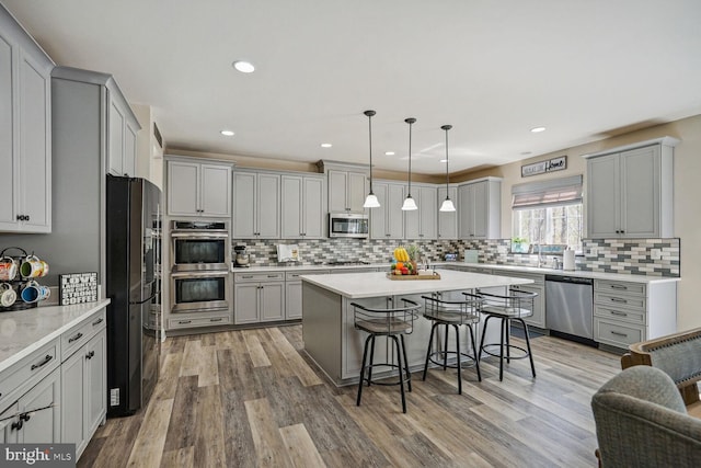 kitchen featuring backsplash, gray cabinetry, appliances with stainless steel finishes, and a breakfast bar