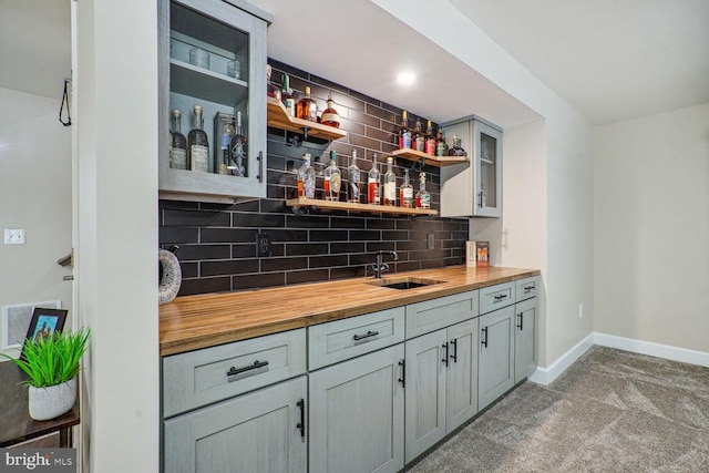 bar featuring carpet flooring, indoor wet bar, baseboards, tasteful backsplash, and a sink