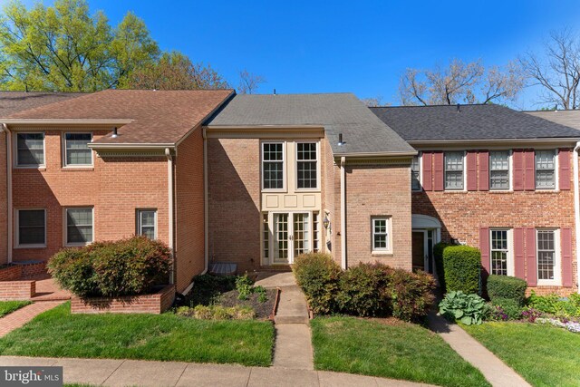 view of front facade featuring brick siding, a shingled roof, and a front yard