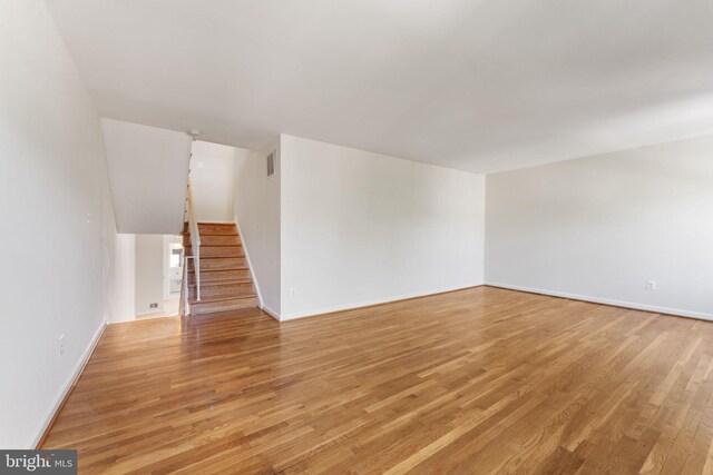 unfurnished living room with baseboards, visible vents, stairway, and light wood-style floors