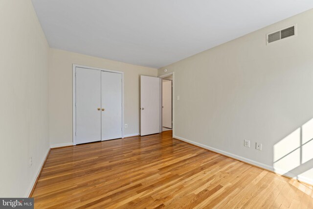 unfurnished bedroom with baseboards, a closet, wood finished floors, and visible vents