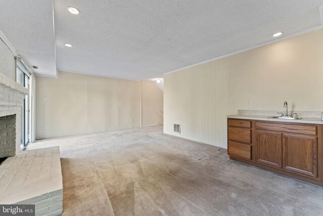 unfurnished living room with light carpet, a sink, a fireplace, a textured ceiling, and visible vents
