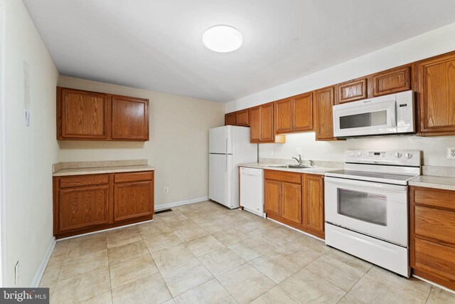 kitchen featuring brown cabinetry, a sink, and white appliances