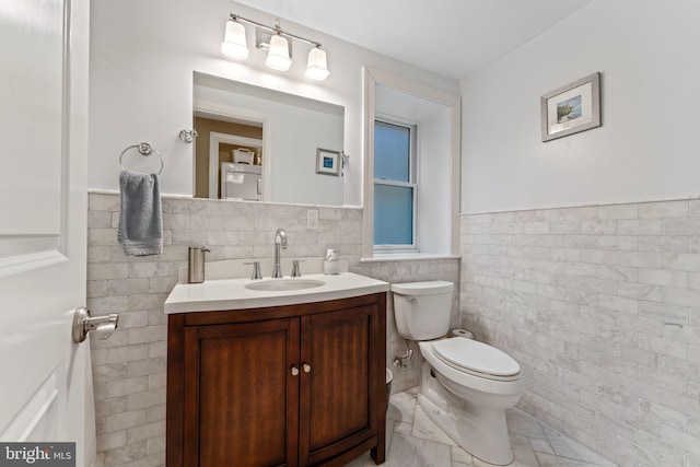 bathroom with toilet, vanity, wainscoting, and tile walls