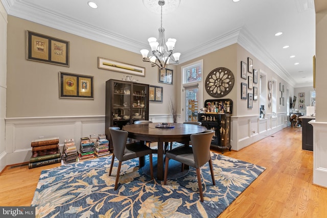 dining room featuring an inviting chandelier, recessed lighting, crown molding, a decorative wall, and light wood finished floors