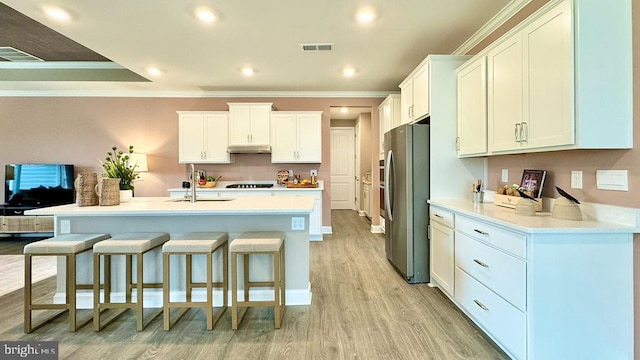 kitchen featuring freestanding refrigerator, crown molding, white cabinets, under cabinet range hood, and visible vents
