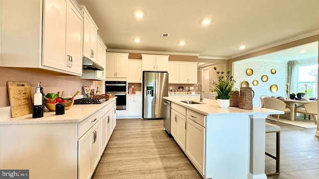 kitchen featuring visible vents, a sink, under cabinet range hood, crown molding, and stainless steel appliances
