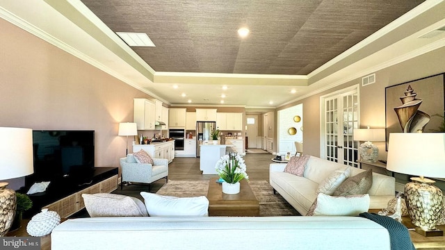 living room with ornamental molding, a tray ceiling, visible vents, and wood finished floors