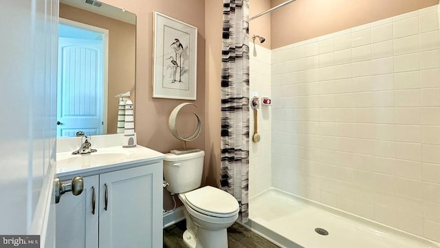 full bath with toilet, a tile shower, vanity, and wood finished floors