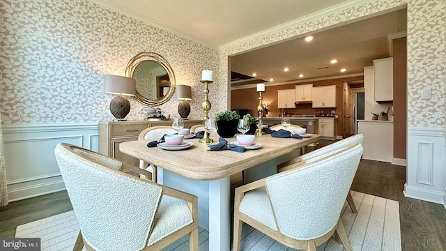 dining room with crown molding, a decorative wall, dark wood-style flooring, wainscoting, and wallpapered walls