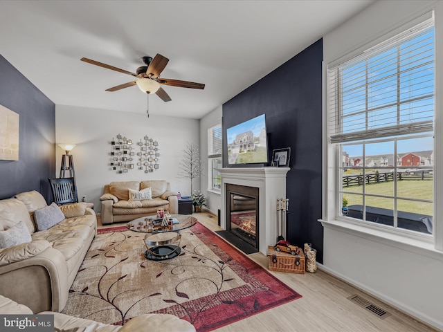 living area with wood finished floors, a ceiling fan, visible vents, and plenty of natural light