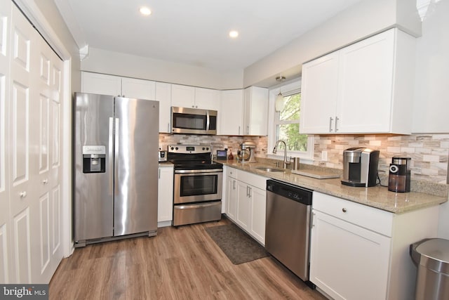 kitchen with wood finished floors, white cabinetry, a sink, appliances with stainless steel finishes, and backsplash