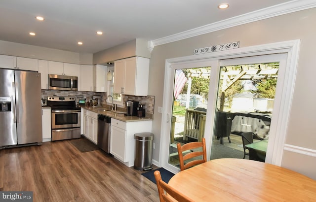 kitchen featuring dark wood-style flooring, crown molding, a sink, white cabinets, and stainless steel appliances