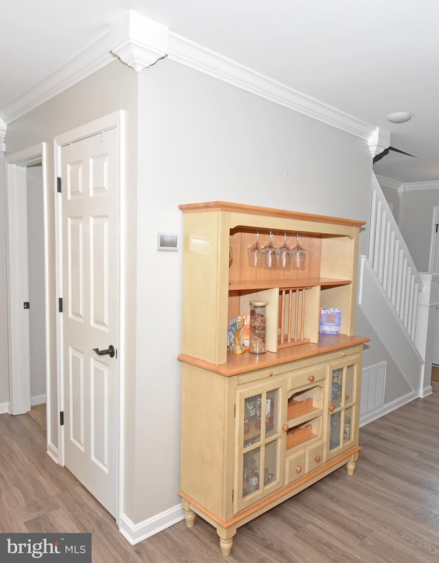 hallway featuring visible vents, wood finished floors, stairway, baseboards, and ornamental molding