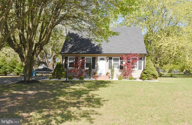 cape cod house with roof with shingles, entry steps, and a front lawn