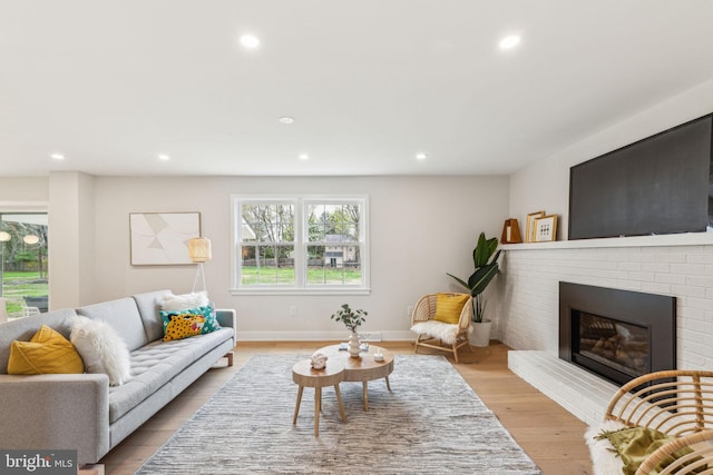 living area with light wood finished floors, baseboards, a brick fireplace, and recessed lighting