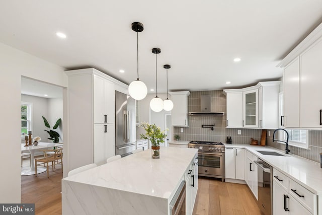 kitchen featuring tasteful backsplash, premium appliances, a sink, wall chimney exhaust hood, and a kitchen island