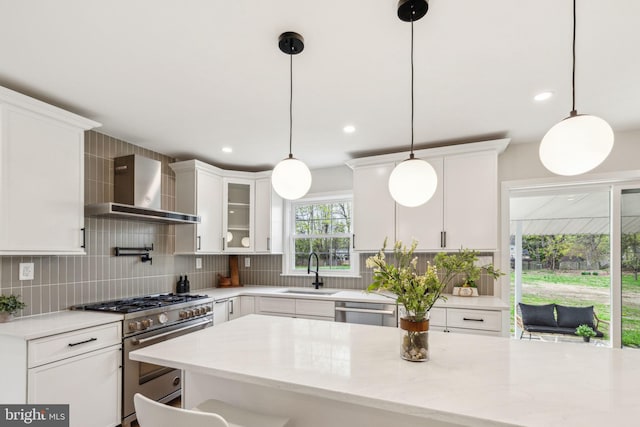 kitchen featuring stainless steel appliances, a sink, backsplash, and wall chimney range hood