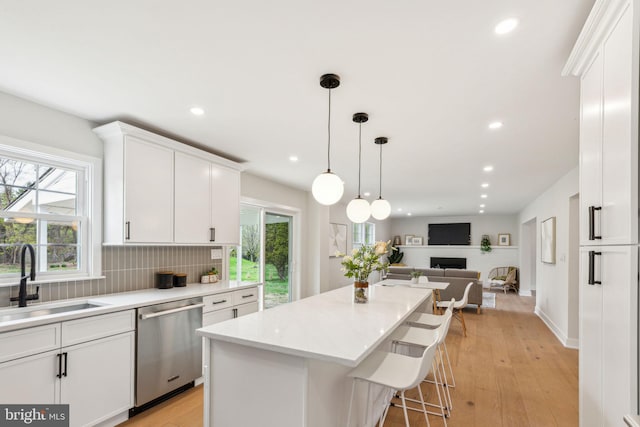 kitchen featuring dishwasher, a sink, a center island, a fireplace, and white cabinetry