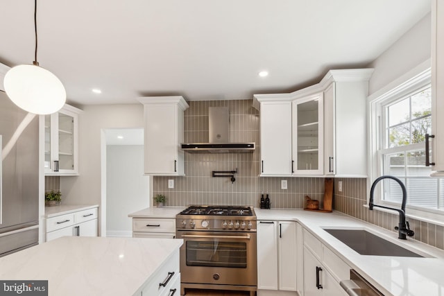 kitchen with wall chimney exhaust hood, stainless steel appliances, a sink, white cabinetry, and decorative backsplash