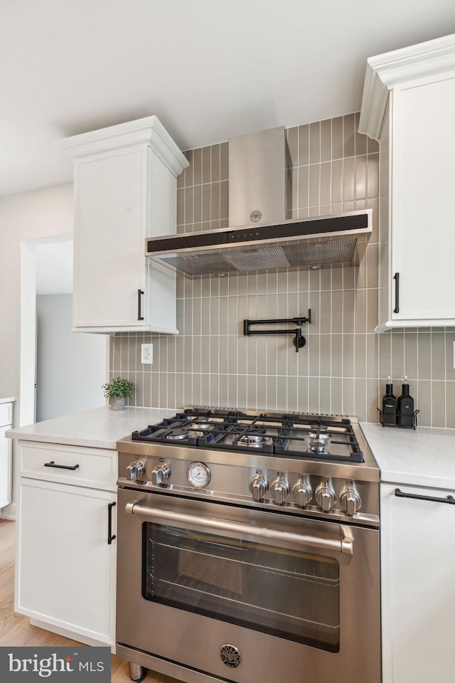 kitchen with white cabinets, high end stainless steel range oven, decorative backsplash, wall chimney range hood, and light countertops