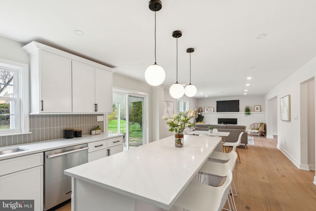 kitchen featuring stainless steel dishwasher, white cabinets, light wood-style floors, backsplash, and a kitchen island