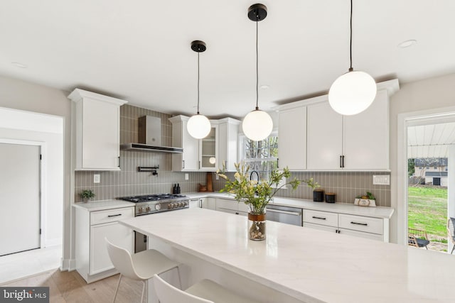 kitchen with backsplash, wall chimney range hood, white cabinets, and stainless steel appliances
