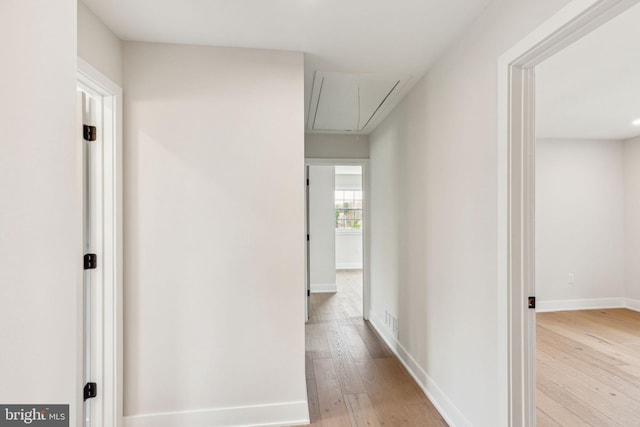 hall featuring light wood finished floors, attic access, baseboards, and visible vents