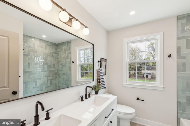 bathroom featuring a tile shower, double vanity, toilet, and a sink