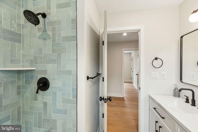 bathroom with baseboards, wood finished floors, vanity, and tiled shower