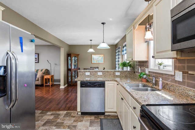 kitchen featuring a peninsula, backsplash, decorative light fixtures, appliances with stainless steel finishes, and a sink